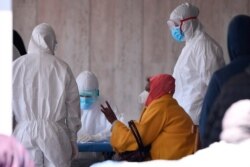 A woman with a face mask speaks with medical staff in protective clothing at a refugee camp after two suspect cases of coronavirus were allegedly confirmed and the area cordoned off as a red zone, on the outskirts of Rome, April 8, 2020.