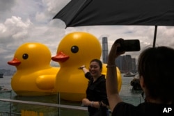Members of the public photograph an art installation called "Double Ducks" by Dutch artist Florentijn Hofman at Victoria Harbour in Hong Kong, Friday, June 9, 2023. (AP Photo/Louise Delmotte)