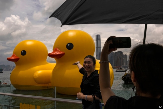 Members of the public photograph an art installation called "Double Ducks" by Dutch artist Florentijn Hofman at Victoria Harbour in Hong Kong, Friday, June 9, 2023. (AP Photo/Louise Delmotte)