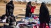 Para perempuan memeriksa baju-baju bekas di luar kamp al-Hol, tempat pengungsian keluarga mantan kombatan ISIS, di wilayah al-Hasakeh, timur laut Suriah, 14 Januari 2020. (Foto: AFP) 