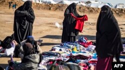 Para perempuan memeriksa baju-baju bekas di luar kamp al-Hol, tempat pengungsian keluarga mantan kombatan ISIS, di wilayah al-Hasakeh, timur laut Suriah, 14 Januari 2020. (Foto: AFP) 