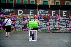 A man holds a sign and the portrait of a victim of femicide in front of a metal fence with the names of other victims surrounding the National Palace ahead of the International Women's Day in Mexico City on March 7, 2021.
