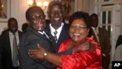 FILE: Zimbabwean President Robert Mugabe, left, celebrates with newly sworn-in vice presidents Joyce Mujuru, right, and the late Joseph Msika, center, State House, Harare, Oct. 2008 file photo.