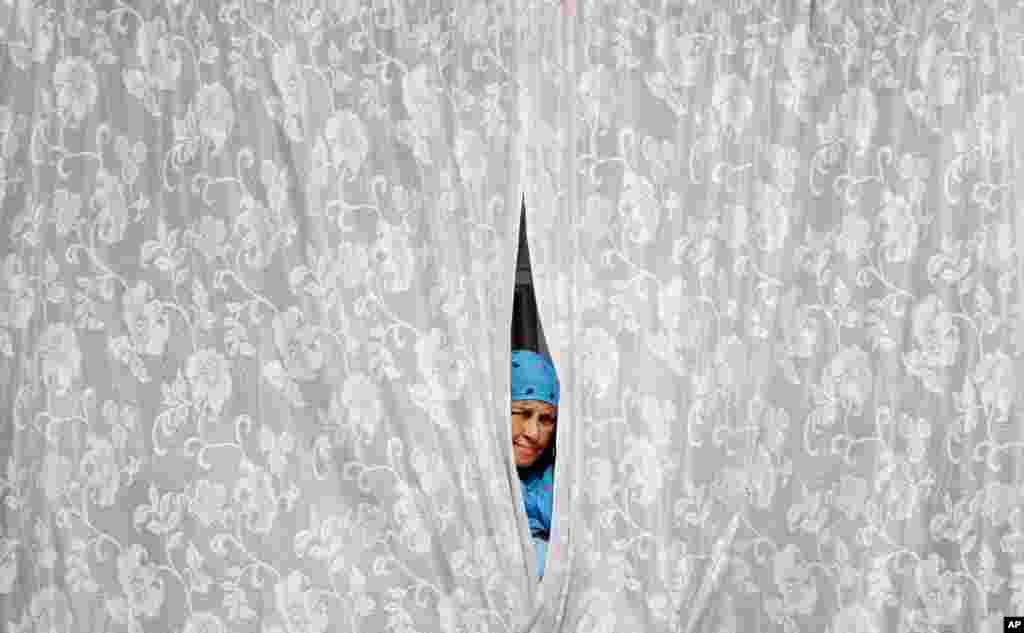 A Kashmiri woman from behind a curtain of a window in Srinagar, India