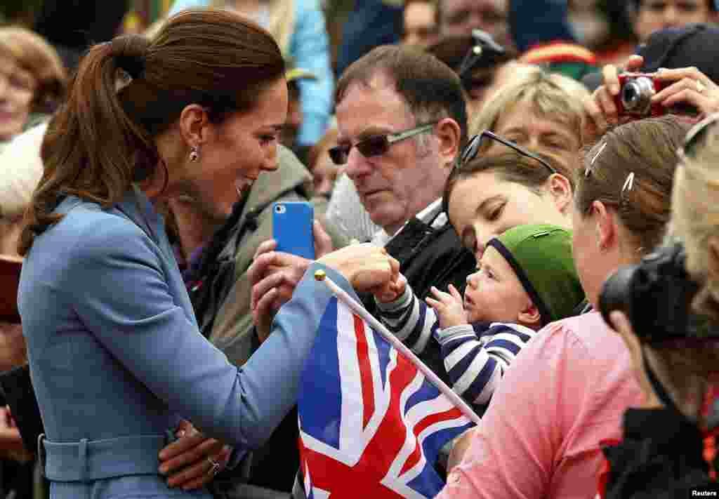 Catherine (L), Duchess of Cambridge, holds the hand of a baby in the crowd after laying a wreath with her husband, Britain&#39;s Prince William, at the war memorial in Seymour Square in the town of Blenheim, New Zealand.