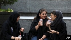 In this July 2, 2019 photo, young women sit outside a shopping mall in northern Tehran.