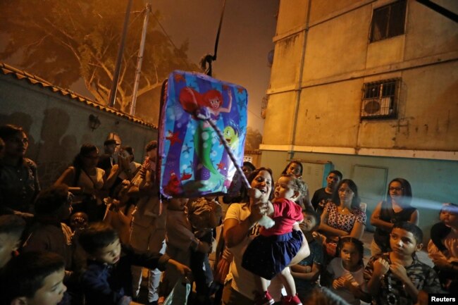 FILE - A woman holds a child as they get ready to hit a pinata at a birthday party celebration in Caracas, Venezuela, April 13, 2019.