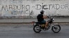 FILE - A man on a motorcycle rides past a mural that reads, "Maduro. Dictator. Resign" during a blackout in Caracas, Venezuela, March 27, 2019.