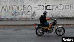 FILE - A man on a motorcycle rides past a mural that reads, "Maduro. Dictator. Resign" during a blackout in Caracas, Venezuela, March 27, 2019.