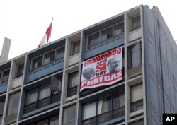 A protest banner that shows images of Pope Francis and Cardinal Sean O'Malley with a message that reads in Spanish: "Francisco, here we do have proof", hangs from a building located outside the Shrine of Our Lord of the Miracles, in Lima, Jan. 21, 2018.