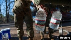 National Guard sergeants fill gallons for a resident at a public water distribution site after a recent bout of cold weather caused large numbers of water outages, some going into their third week, in Jackson, Mississippi, March 4, 2021. 