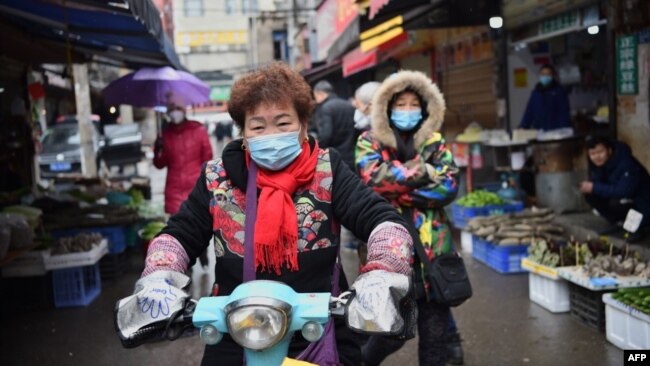 资料照片:一名戴着口罩的妇女骑着电动车穿过武汉市的一个市场。（2020年1月24日）