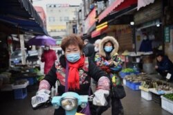 一名戴着口罩的妇女骑着电动车穿过武汉市的一个市场。（2020年1月24日）
