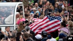 Faithful display a flag of the United States as Pope Francis kisses an infant from his pope-mobile during his tour through the crowd for his weekly general audience in St. Peter's Square at the Vatican, March 23, 2016.
