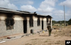 A member of Kenya's security forces walks past a damaged police post after an attack by al-Shabab extremists in the settlement of Kamuthe in Garissa county, Kenya Monday, Jan. 13, 2020