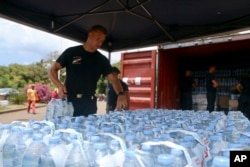 FILE —A security officer picks up water bottles for residents in Tsoundzou, on the French Indian Ocean territory of Mayotte, Saturday Oct. 21, 2023. The crisis is a wakeup call to Paris about the cost of managing climate change across France’s far-flung territories.