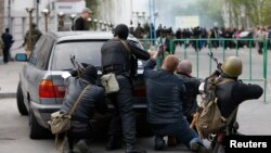 Pro-Russian armed men take cover behind a car near the local police headquarters in Luhansk, eastern Ukraine, April 29, 2014. 