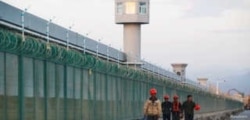 FILE - Workers walk by the perimeter fence of what is officially known as a vocational skills education center in Dabancheng, in Xinjiang Uighur Autonomous Region, China, Sept. 4, 2018.