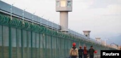 FILE - Workers walk by the perimeter fence of what is officially known as a vocational skills education center in Dabancheng, in Xinjiang Uighur Autonomous Region, China, Sept. 4, 2018.