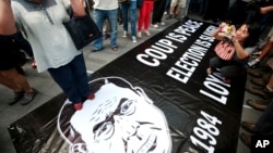 Protesters stand and take a photograph on a defaced poster of Thai Army Chief Gen. Prayuth Chan-ocha during an anti-coup demonstration in Bangkok, Thailand, June 1, 2014.