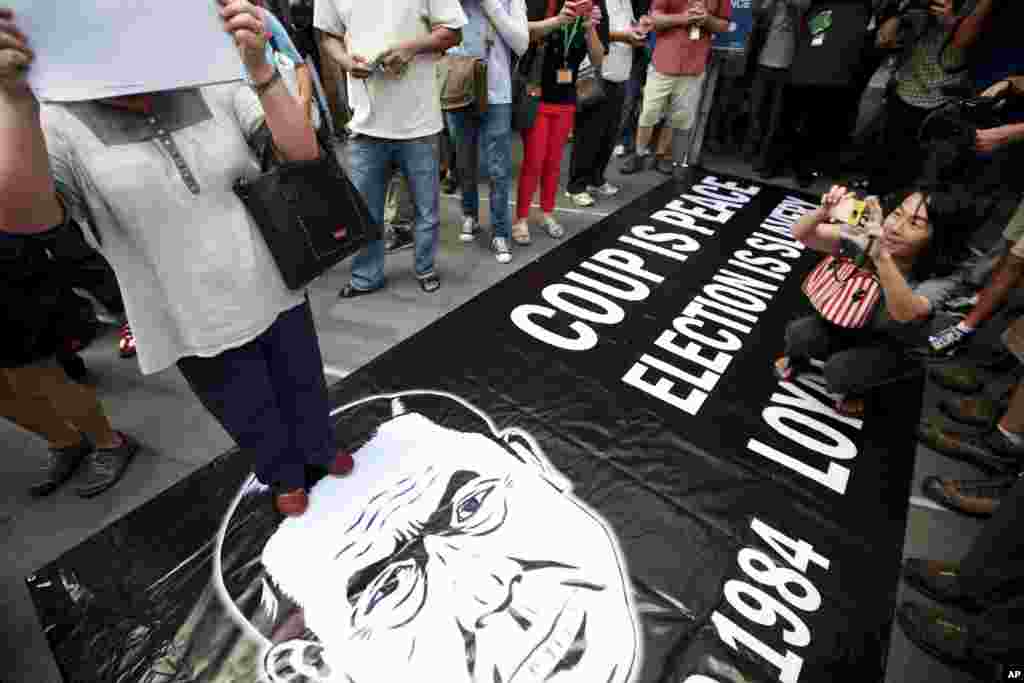 Para demonstran berdiri dan berfoto di atas poster Kepala Angkatan Darat Thailand Jenderal Prayuth Chan-ocha dalam sebuah demonstrasi anti-kudeta di Bangkok, Thailand (1/6).