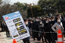 An employee holds a board with information of face mask sales as people line up to buy face masks to protect themselves from the new coronavirus outside Nonghyup Hanaro Mart in Seoul, South Korea, March 5, 2020.