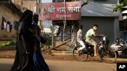 Perempuan muslim tak dikenal berjalan melewati papan yang menampilkan nama kelompok nasionalis Hindu Sri Ram Sena Hindustan di lingkungan perumahan di Belagavi, India, 7 Oktober 2021. (AP Photo/Aijaz Rahi).