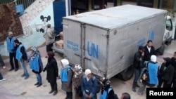 U.N. Relief and Works Agency (UNRWA) workers stand by aid parcels at the Palestinian refugee camp of Yarmouk, south of Damascus in this picture made available on February 26, 2014. World powers have passed a landmark Security Council resolution demanding 