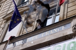 FILE - An activist member of Extinction Rebellion (XR) hold up a smoke flare while standing on the balcony of the Banque de France during a protest to denounce investments in fossil fuels, in Paris, Apr. 1, 2021.