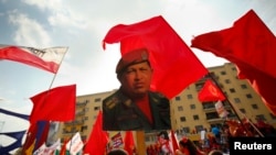 FILE - A supporter of Venezuela's President Nicolas Maduro holds up a picture of late president Hugo Chavez during a May Day demonstration in Caracas, May 1, 2014. 