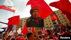 FILE - A supporter of Venezuela's President Nicolas Maduro holds up a picture of late president Hugo Chavez during a May Day demonstration in Caracas, May 1, 2014. 