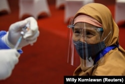 Seorang perempuan yang memakai masker dan pelindung wajah terlihat saat petugas kesehatan bersiap untuk menyuntiknya dengan vaksin Sinovac selama program vaksinasi massal COVID-19 di Bursa Efek Indonesia di Jakarta, 31 Maret 2021. (Foto: REUTERS/Willy Kur