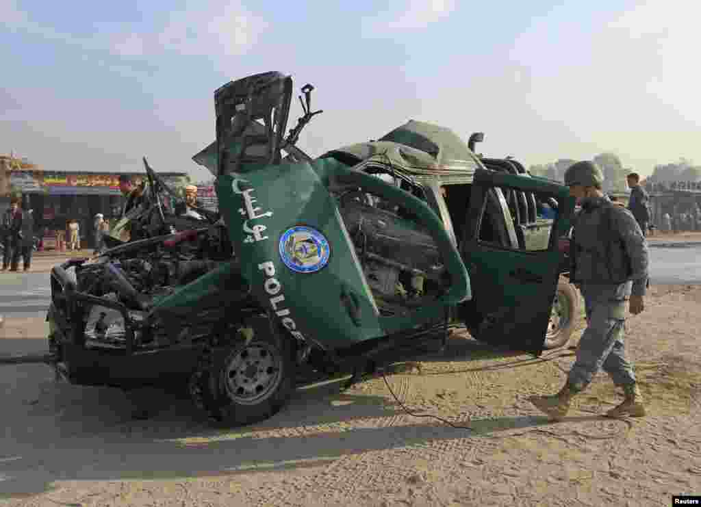 An Afghan policeman inspects the wreckage of a police car that was destroyed by a magnetic bomb attached to the car, in Jalalabad, Dec. 17, 2014.