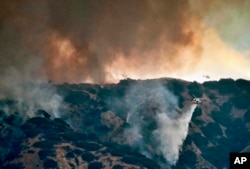 A helicopter makes a water drop amid black smoke rising from a wildfire burning in the Tujunga area of Los Angeles, seen from nearby Burbank, Calif., Sept. 1, 2017. Subdivisions full of houses are within a mile of the flames, and residents have been told to evacuate.