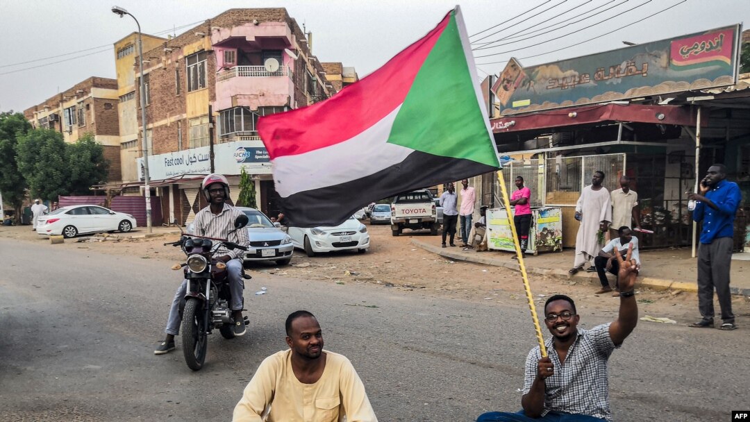 A Sudanese man sits with another in a street while waving a national flag during a mass demonstration against the country's ruling generals in the capital Khartoum, June 30, 2019. 