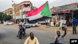 A Sudanese man sits with another in a street while waving a national flag during a mass demonstration against the country's ruling generals in the capital Khartoum, June 30, 2019. 