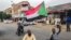 A Sudanese man sits with another in a street while waving a national flag during a mass demonstration against the country's ruling generals in the capital Khartoum, June 30, 2019. 