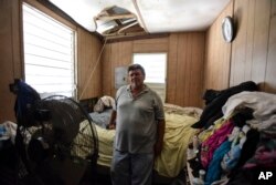 FILE - Moises Valentin poses for a photo in his home damaged by Hurricane Maria, where the U.S. Army Corps of Engineers built him a temporary roof, in San Juan, Puerto Rico, Oct. 19, 2017.
