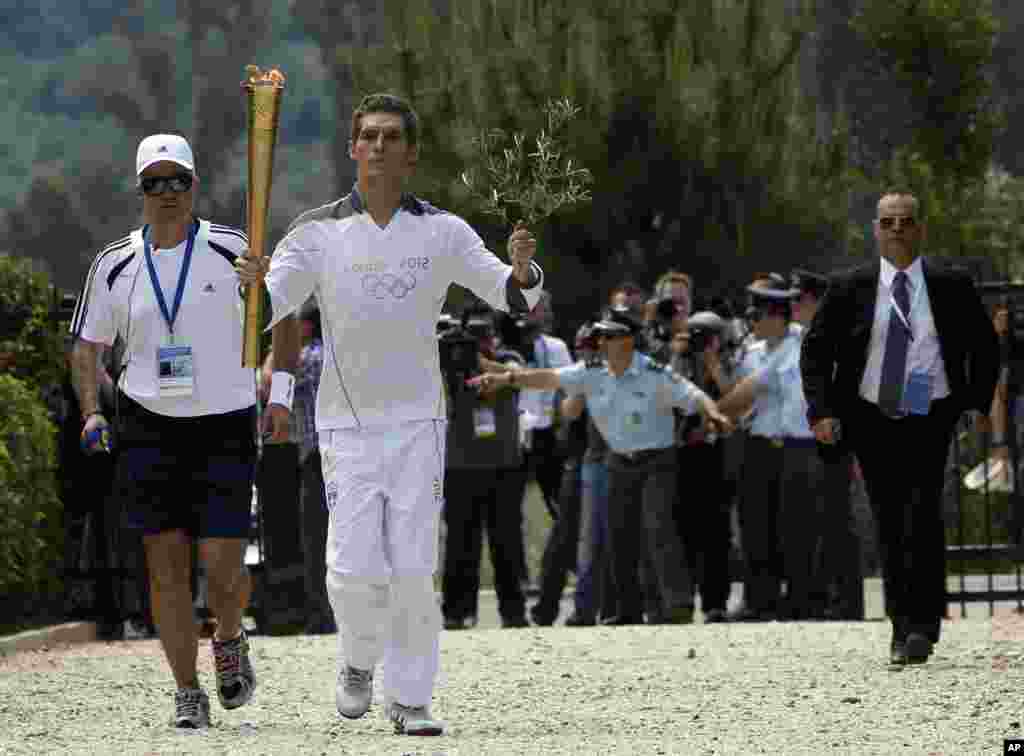 Spyridon Gianniotis, Greece&#39;s world champion of swimming, runs with the Olympic flame and an olive branch during the Olympic torch relay.