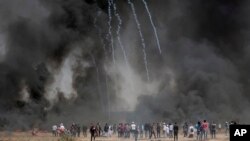 Palestinian protesters gather in front of burned tires while Israeli soldiers fire teargas during clashes with Israeli troops along Gaza's border with Israel, east of Khan Younis, Gaza Strip, Friday, April 6, 2018.