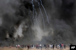 Palestinian protesters gather in front of burned tires while Israeli soldiers fire tear gas during clashes with Israeli troops along Gaza's border with Israel, east of Khan Younis, Gaza Strip, April 6, 2018.