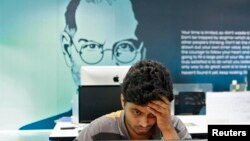 Un empleado trabaja con el fondo de un cartel del fundador de Apple, Steve Jobs, en la ciudad sureña de Kochi, en la India.