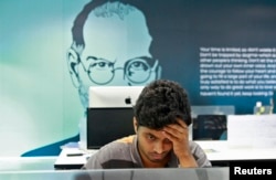 FILE - An employee works on a computer terminal against the backdrop of a picture of late Apple co-founder Steve Jobs at the Start-up Village in Kinfra High Tech Park in the southern Indian city of Kochi.