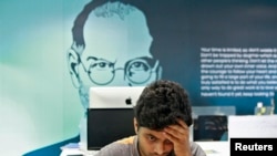 FILE - An image of Steve Jobs looks over the shoulder of computer workers in Kochi, India