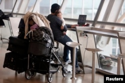 FILE - A passenger holds a baby as he uses his laptop in Israel's Ben-Gurion International Airport near Tel Aviv, April 21, 2013. Men with strollers and on playgrounds are a more common sight now than in their father's generation.