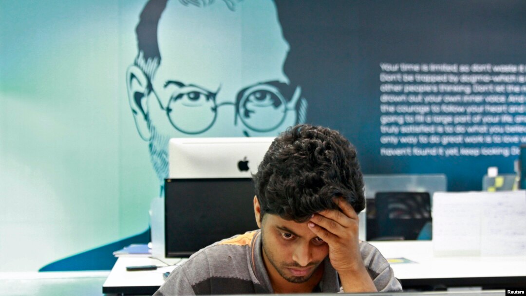 Un empleado trabaja con el fondo de un cartel del fundador de Apple, Steve Jobs, en la ciudad sureña de Kochi, en la India.