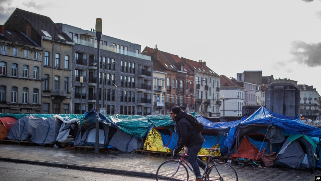 Un hombre pasa en bicicleta frente a un campamento de tiendas de campaña improvisado cerca del centro de recepción del Petit Chateau en Bruselas, Bélgica, el martes 17 de enero de 2023.