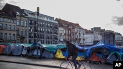 Un hombre pasa en bicicleta frente a un campamento de tiendas de campaña improvisado cerca del centro de recepción del Petit Chateau en Bruselas, Bélgica, el martes 17 de enero de 2023.