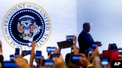 En esta fotografía del 23 de julio de 2019, el presidente Donald Trump sube al estrado en una cumbre juvenil del grupo conservador Turning Point USA en Washington. Sobre el fondo se ve un sello presidencial en el que el águila está agarrando palos de golf en lugar de flechas. 