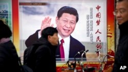 FILE - People walk past a propaganda billboard showing Chinese President Xi Jinping on a street in Beijing, China, March 2, 2018.